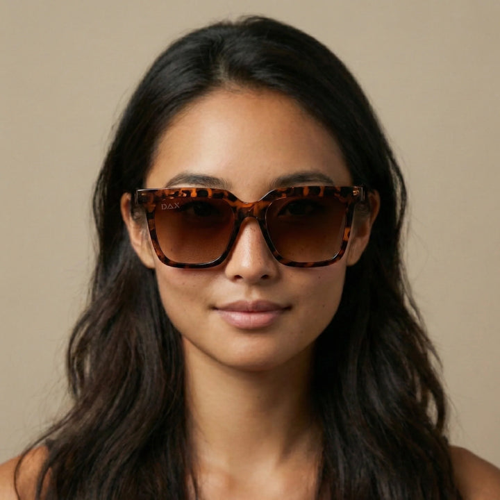 Woman wearing tortoiseshell sunglasses against a neutral background