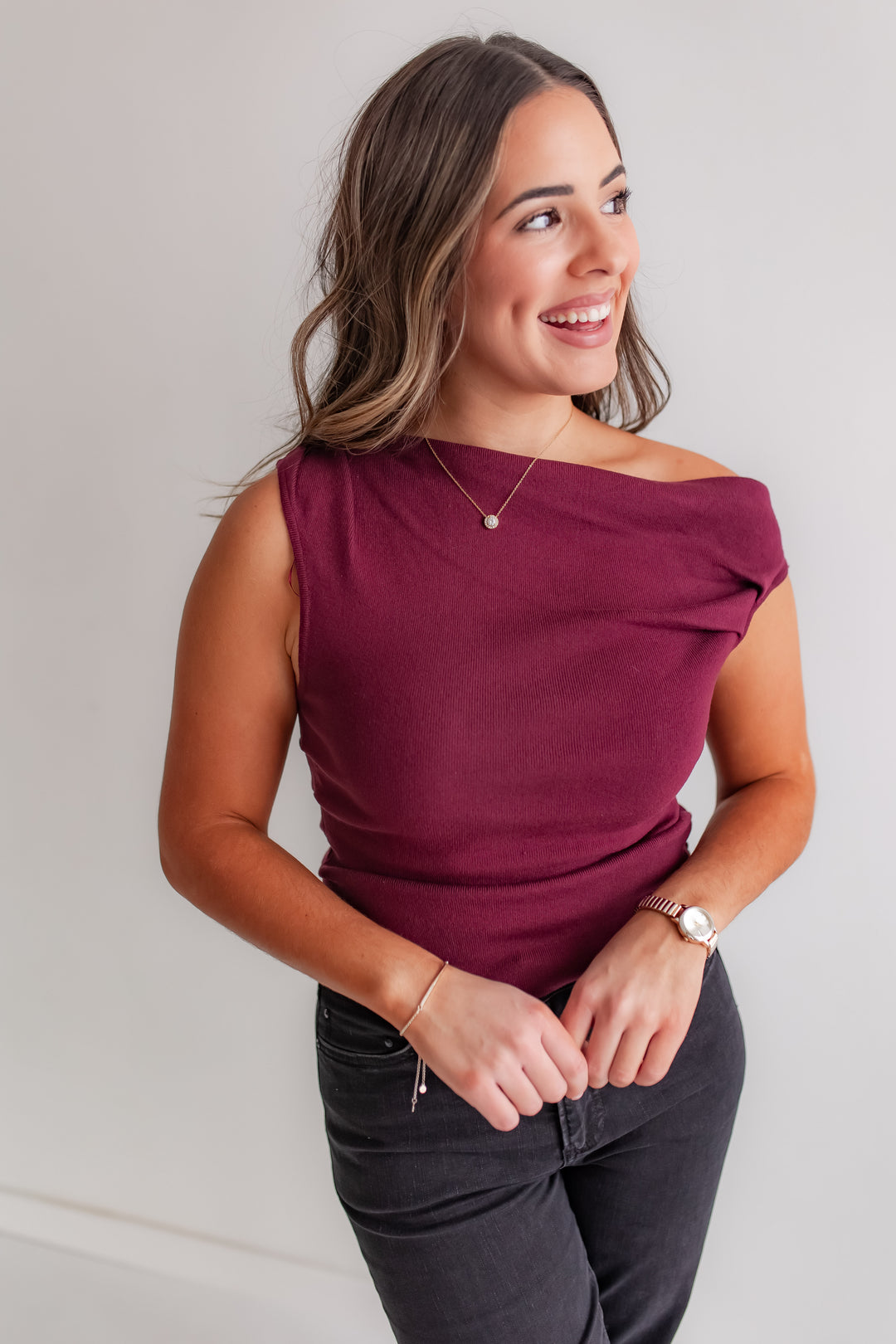 Woman wearing a burgundy asymmetrical top and dark jeans against a plain background
