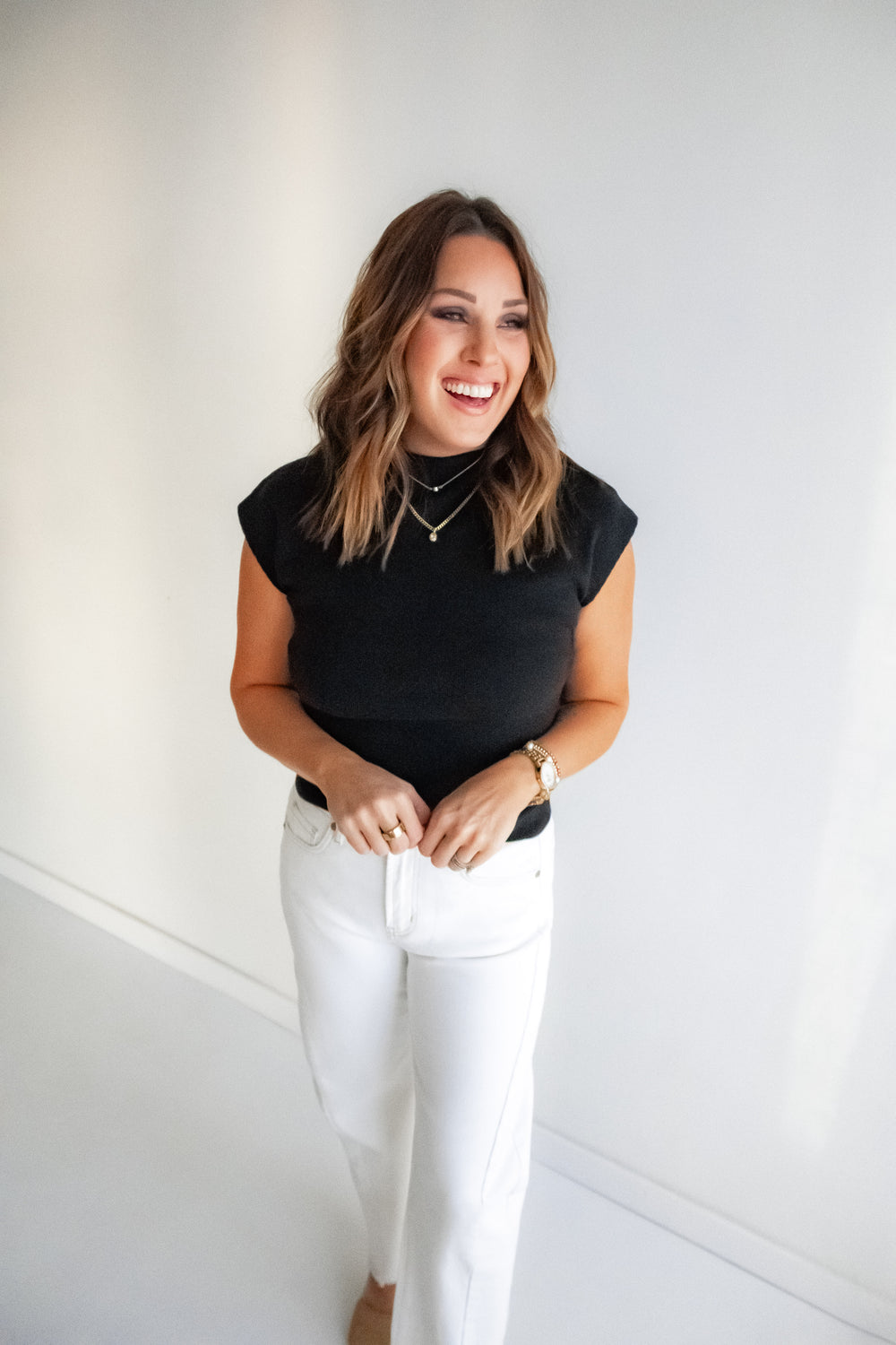 Woman wearing a black, classic cap sleeve top styled with white denim