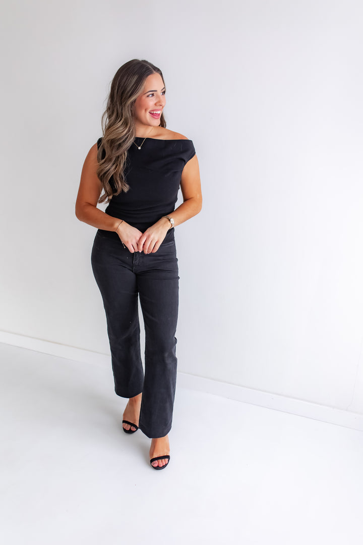 Woman wearing a black off-shoulder top and black pants against a white background