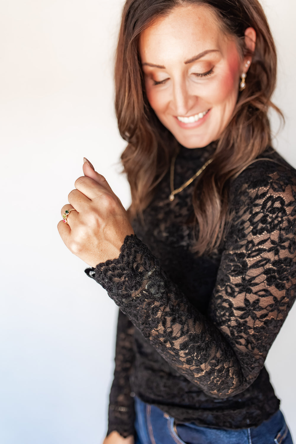 Close-up of black floral lace top with mock neckline and gold pendant necklace