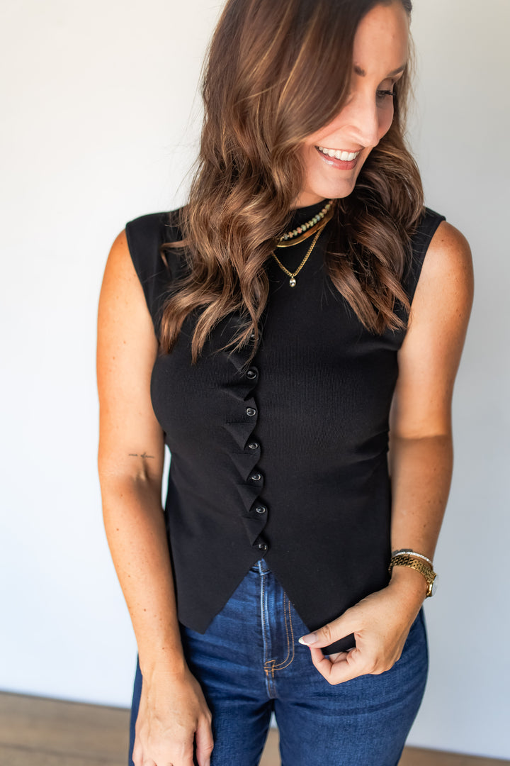 Close-up of black button placket top with layered gold necklaces, smiling