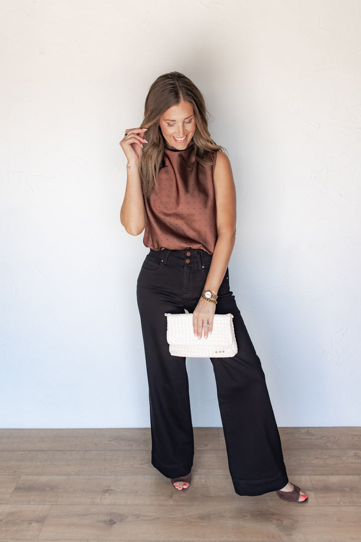 Woman wearing brown polka dot satin top with draped cowl neckline and black jeans