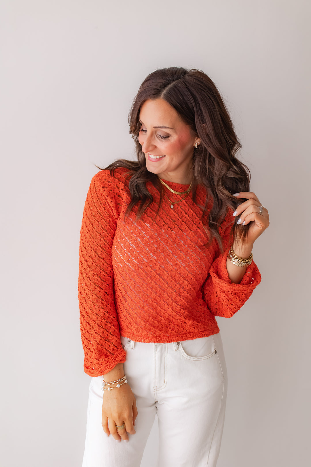 Woman wearing coral open knit sweater styled with white jeans for spring