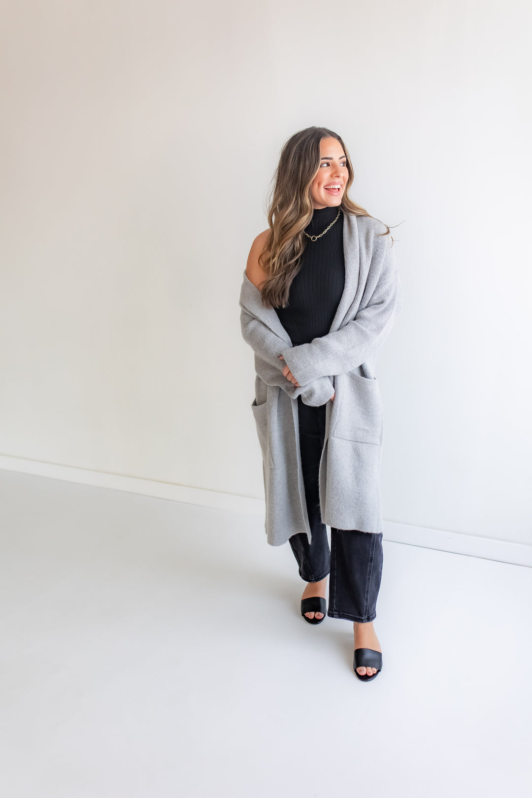 Woman wearing a gray cardigan over a black top and pants on a white background