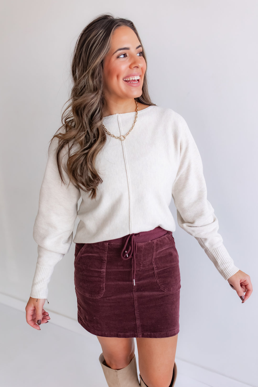 Woman wearing a cream sweater and burgundy corduroy skirt. 