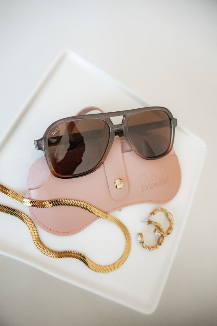 Sunglasses with a pink case and gold chain on a white surface