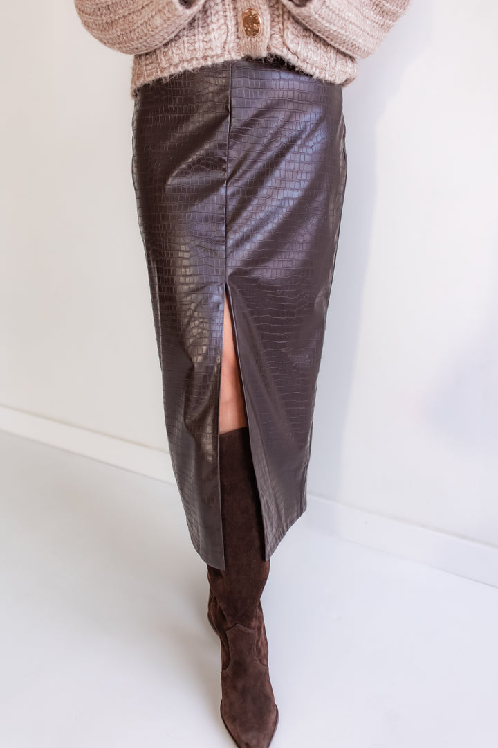 Woman wearing a dark brown croc midi skirt with a high slit and brown knee-high boots