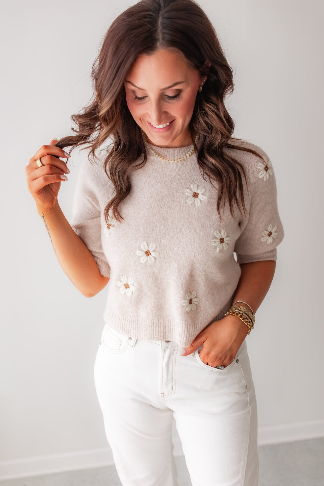 A cream knit sweater with daisy floral appliqué styled with white denim