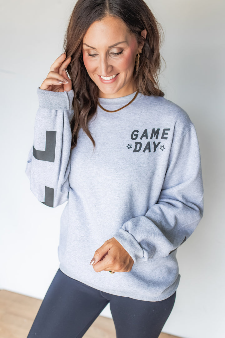 Woman wearing heather gray Game Day sweatshirt with black leggings