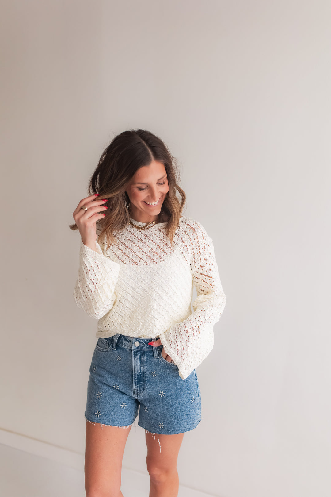 Woman wearing an ivory open knit sweater styled with denim shorts for a casual spring outfit.