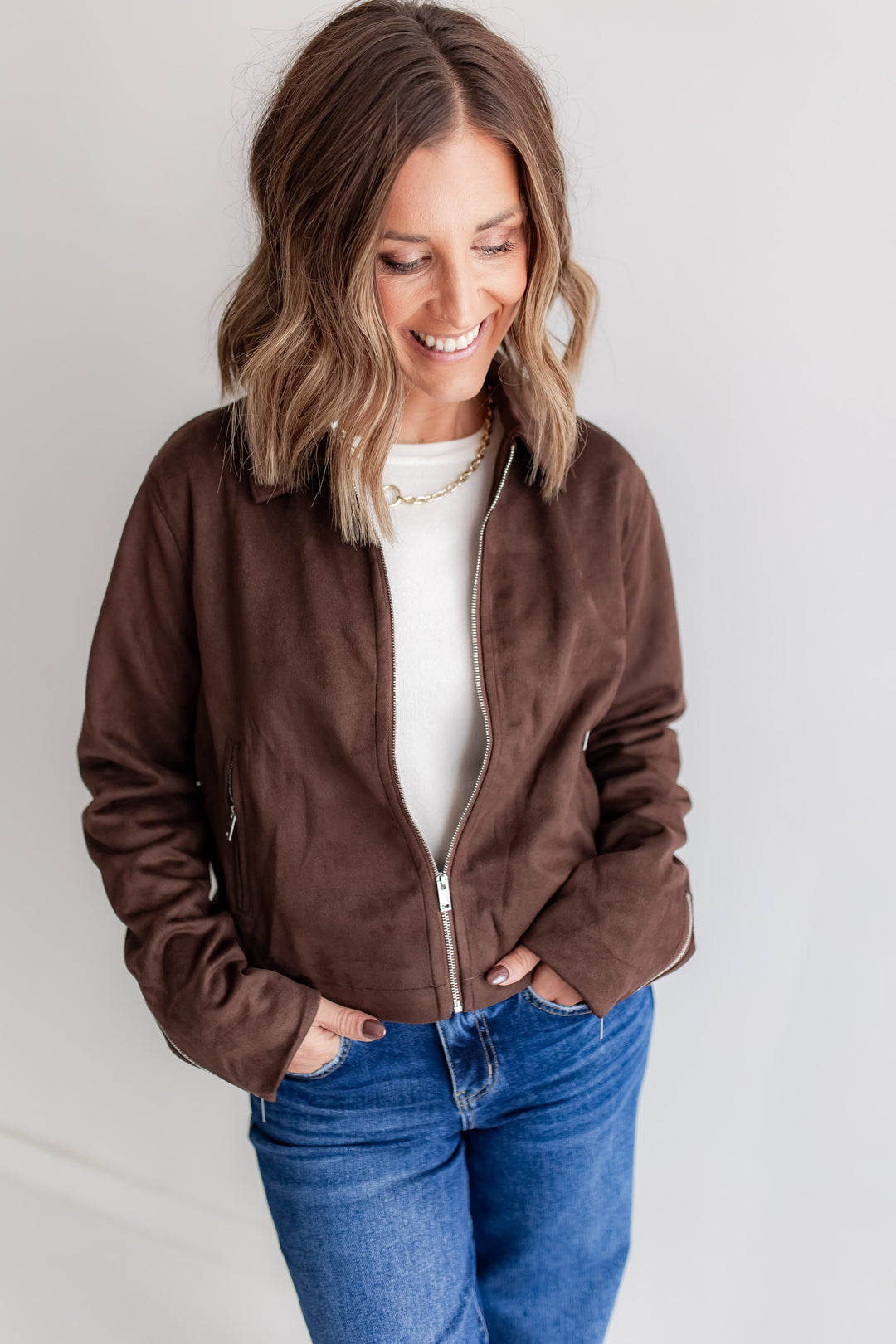 Woman wearing a brown suede jacket, white shirt, and blue jeans