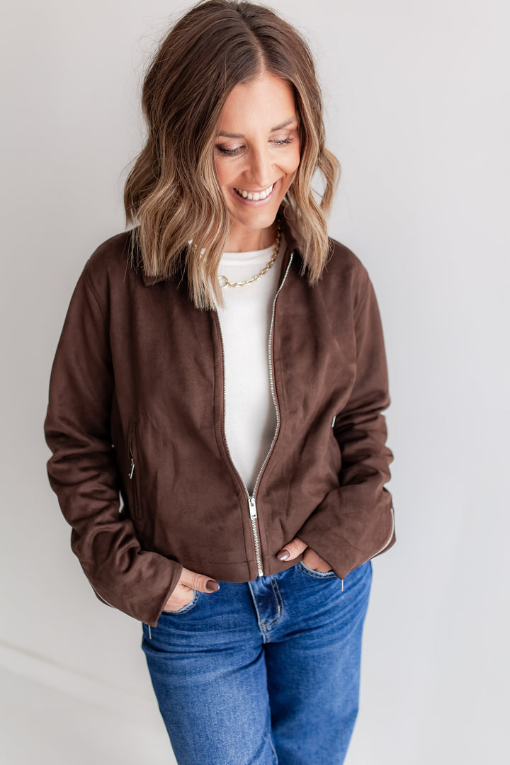 Woman wearing a brown suede jacket, white shirt, and blue jeans