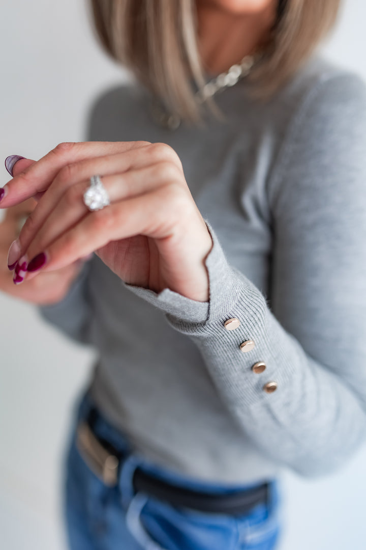Woman wearing a gray lightweight sweater with gold buttons on the cuff.