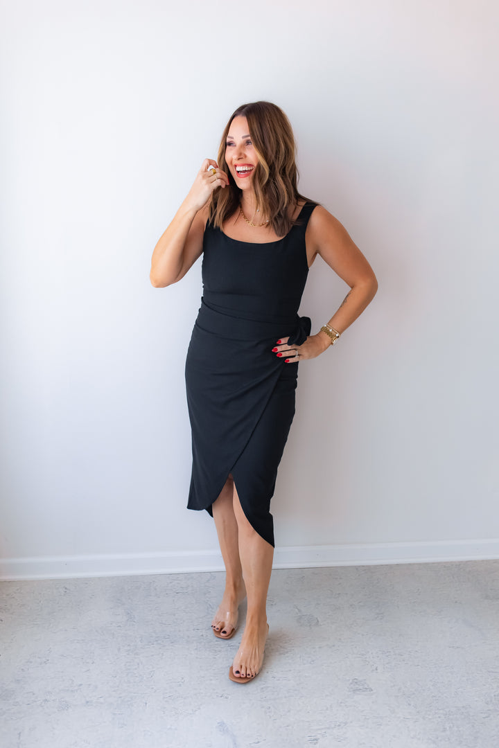 Woman wearing a fitted black wrap midi dress for date night or wedding guest outfit