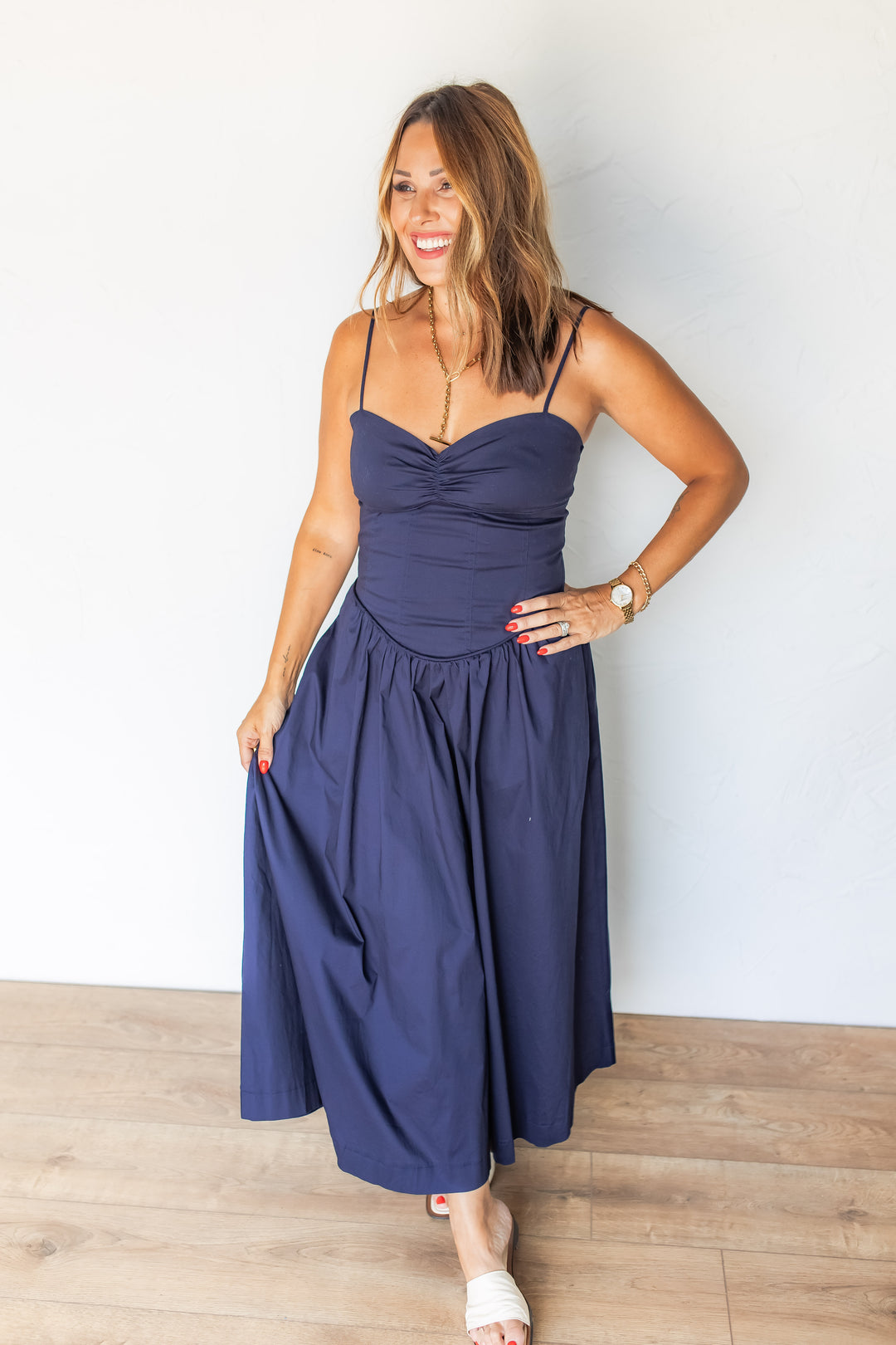 Woman wearing navy corset midi dress with white sandals, smiling