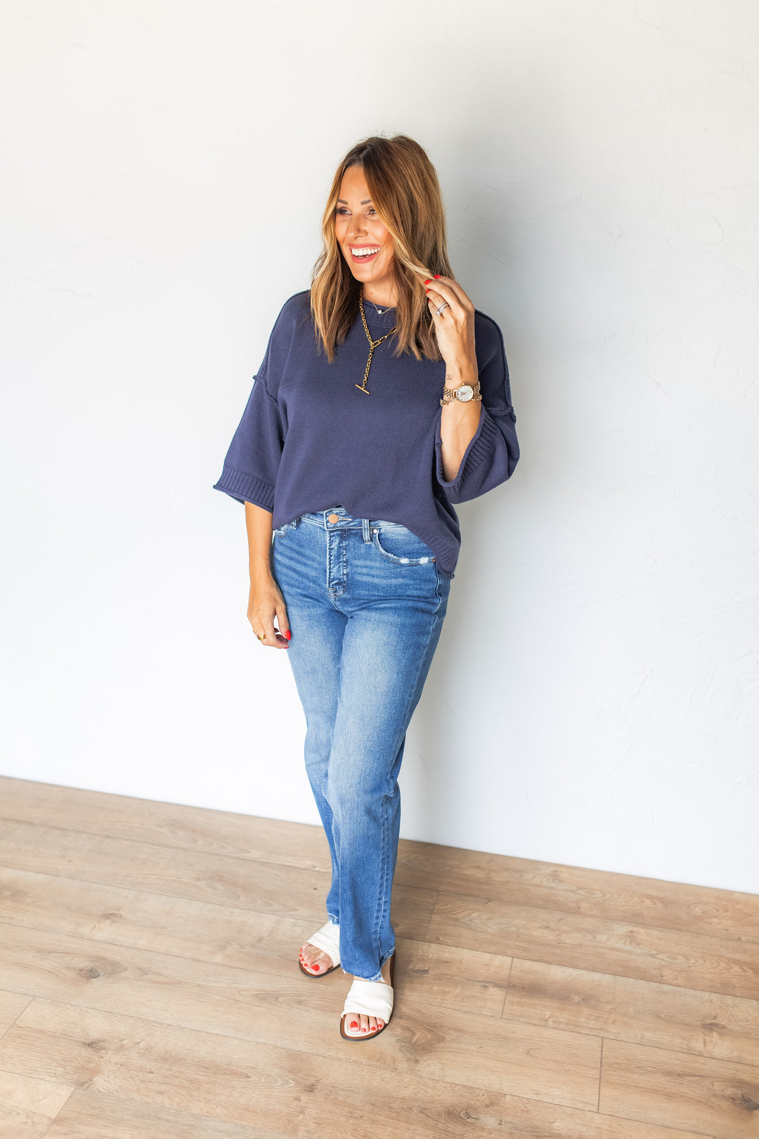 Woman wearing navy short sleeve sweater top styled with medium washed straight jeans and sandles