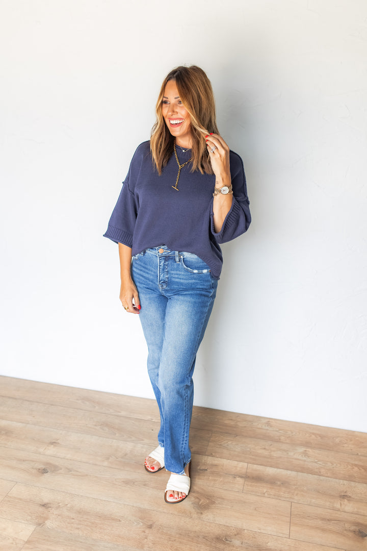 Woman wearing navy short sleeve sweater top styled with medium washed straight jeans and sandles