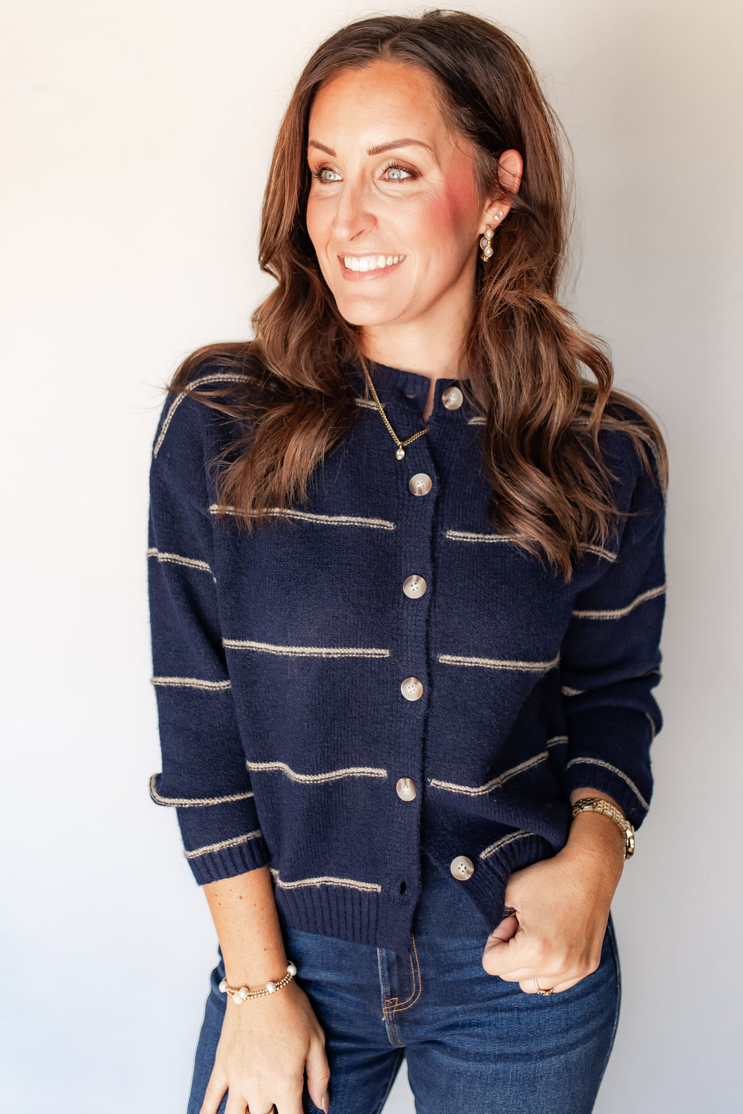 Woman wearing navy striped button-front sweater with pearlescent buttons and denim