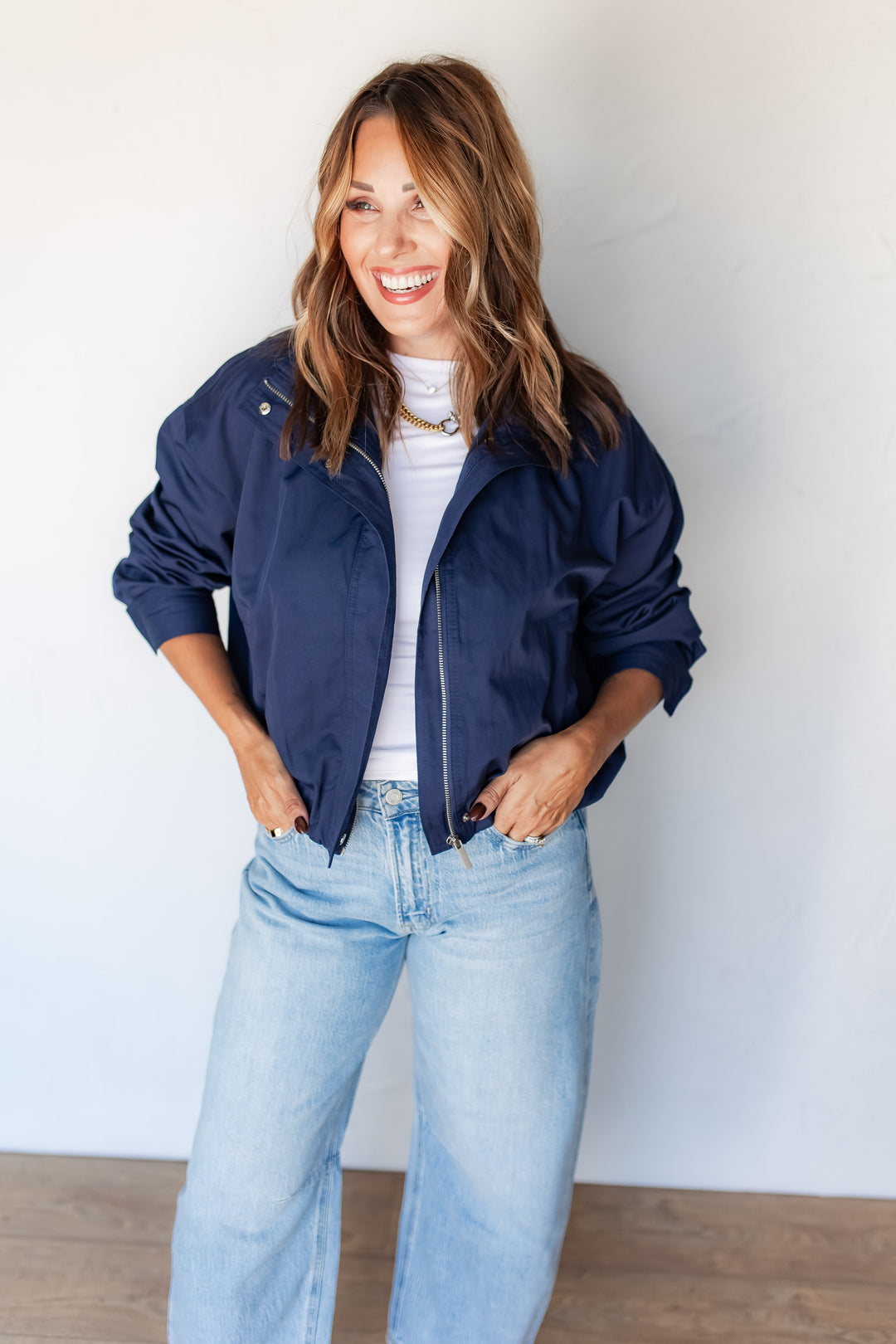 Woman wearing navy cropped zip jacket with funnel collar and light wash jeans
