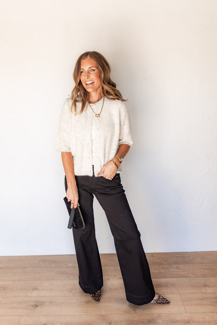 Woman wearing oatmeal button-front sweater with black denim and heels