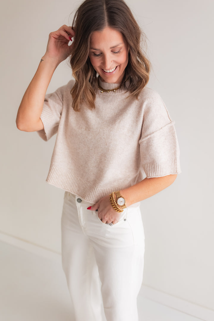 Woman wearing an oatmeal mock neck short sleeve sweater styled with denim for a casual everyday outfit