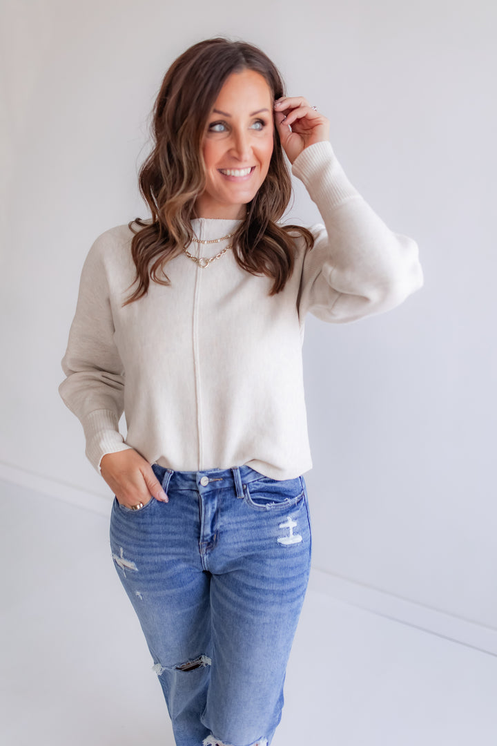 Woman wearing a beige sweater and blue jeans against a white background