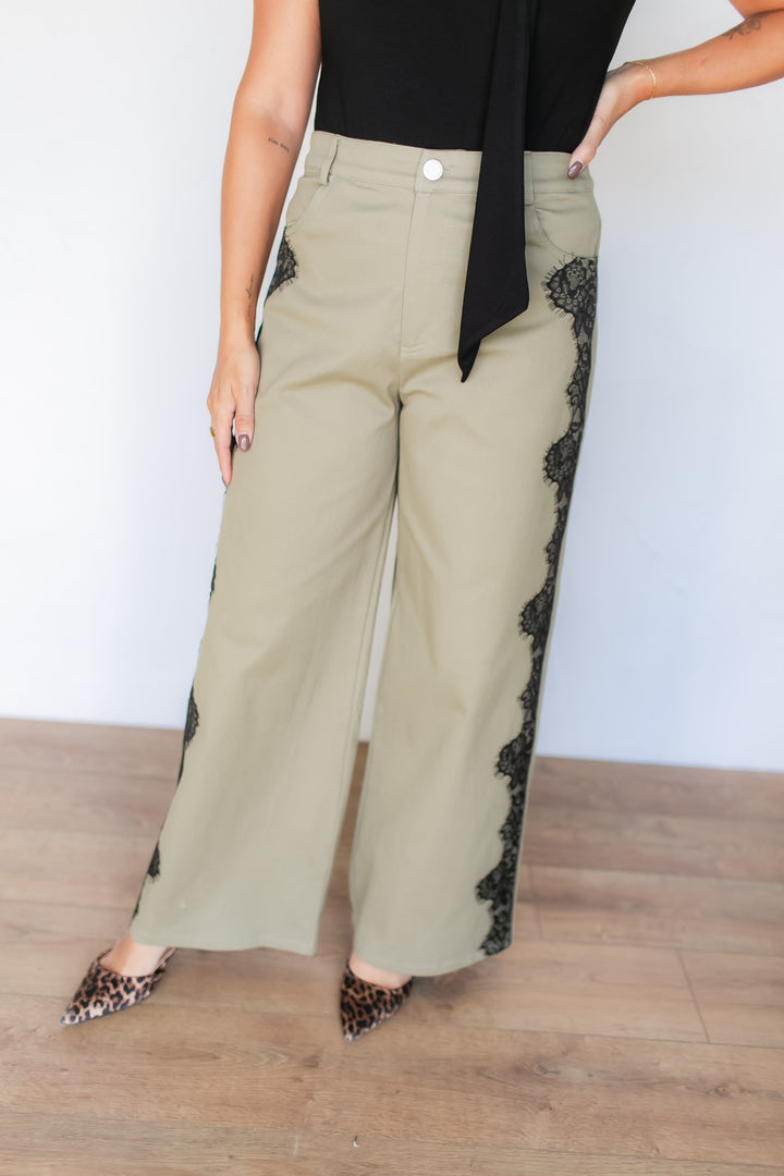 Woman wearing sage green wide leg pants with black lace appliqué detail, styled with a black top