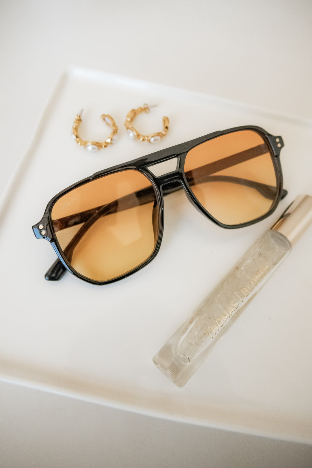 Skye sunglasses with a yellow lens with gold earrings. 