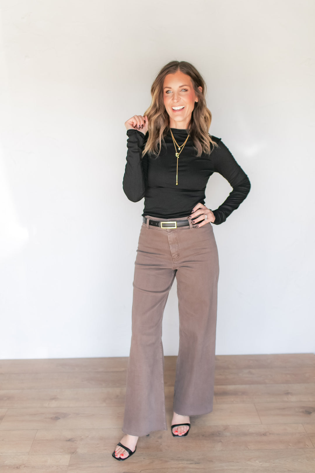 Woman wearing taupe brown wide leg denim trousers with a black turtleneck long sleeve top and black heals