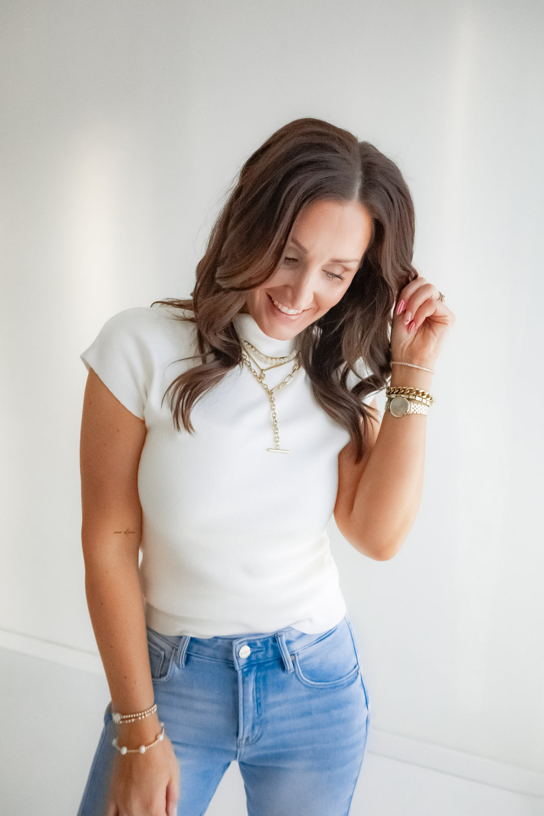 Woman wearing a white wide neck cap sleeve top and blue jeans against a plain background