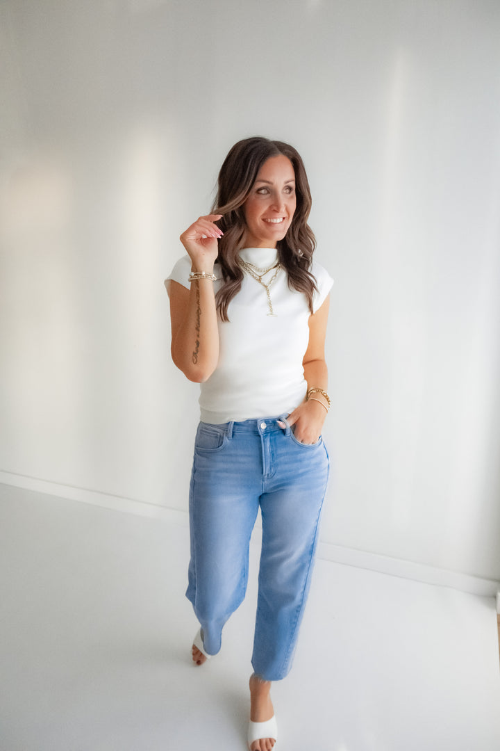 Woman wearing a white top and blue jeans against a plain white wall